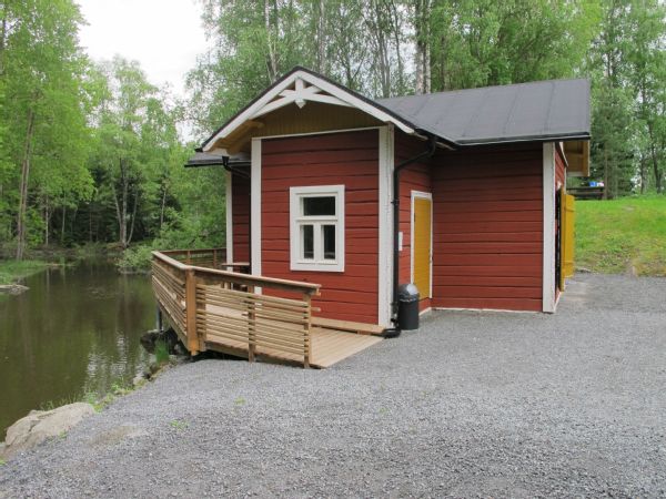 Pieni puurakennus ja terassi joen rannalla.